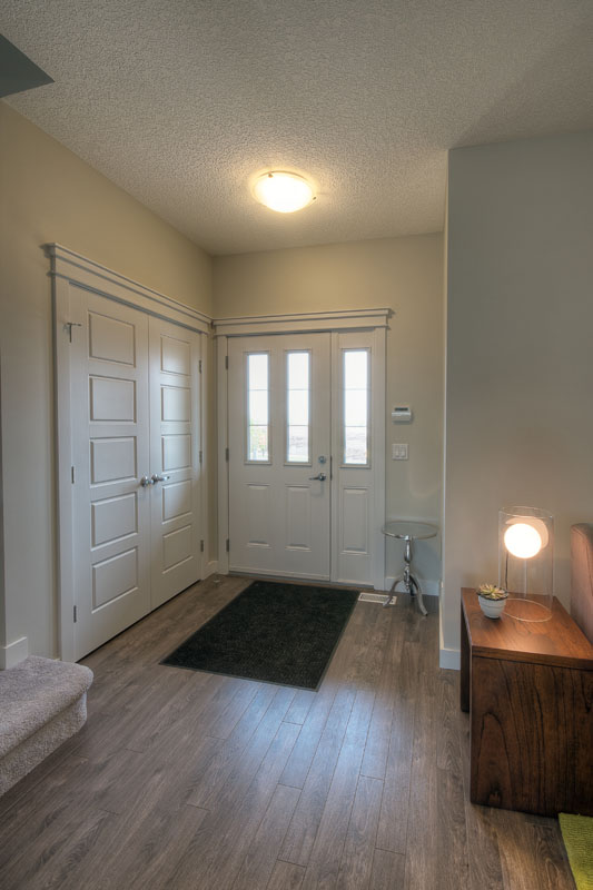 Foyer facing the door with light wood grain plank flooring and a small black rug in the Banbury II model home.