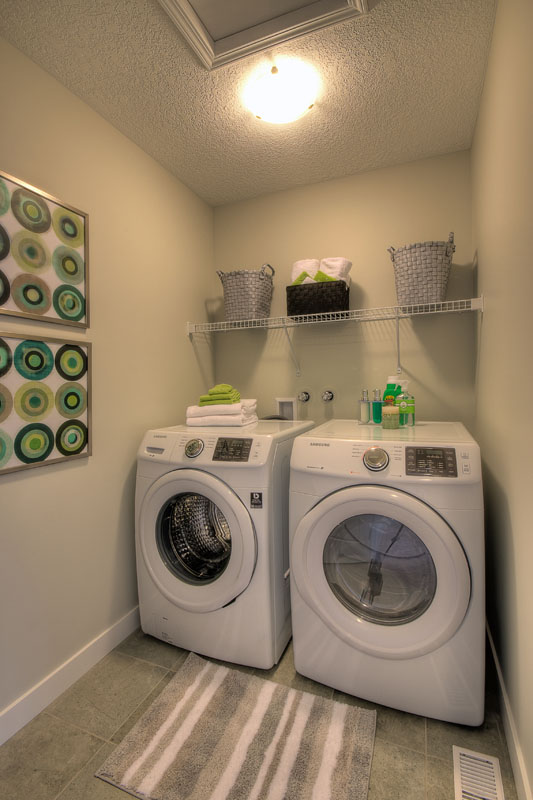 Laundry room with white LG washer and dryer and decrotive green paintings and washing supplies in the Banbury II model home from Nuvista Homes.