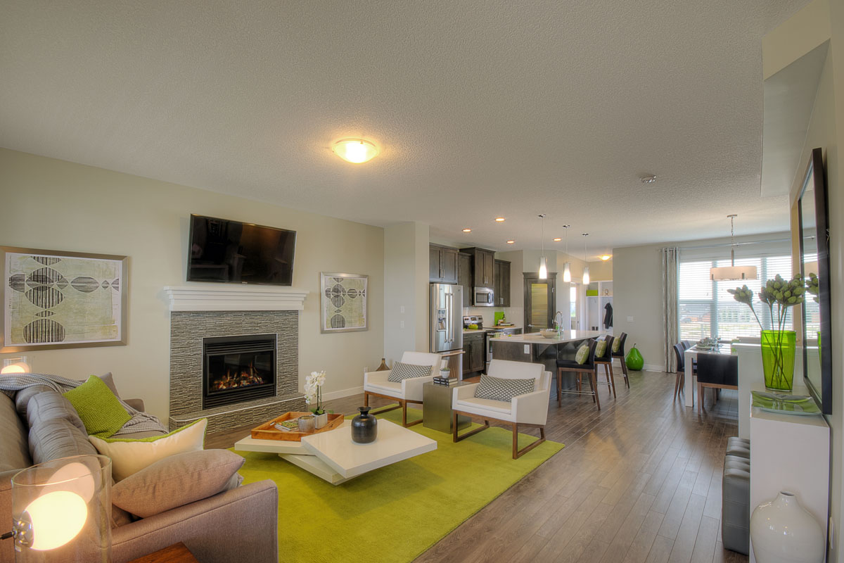 Wide angle shot of the living room and kitchen in the Banbury II home from Nuvista Homes with green area rug and green home decrotations.