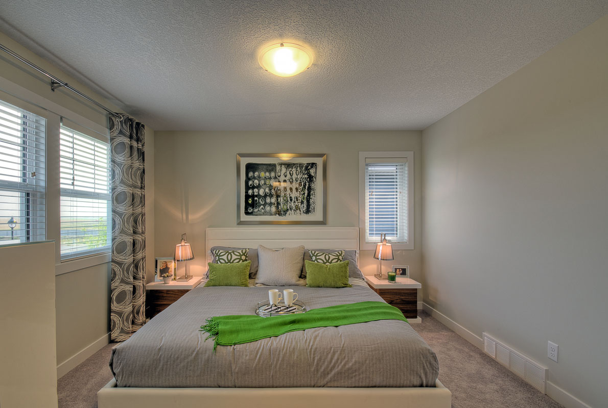 Master bedroom with grey blanket and green throw pillows in between two nightstands in the Banbury II home from Nuvista Homes.