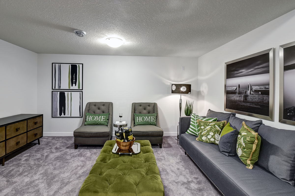 Basement living room in the Banbury II home from Nuvista Homes with green swede bench and grey couch with green decrotive throw pillows