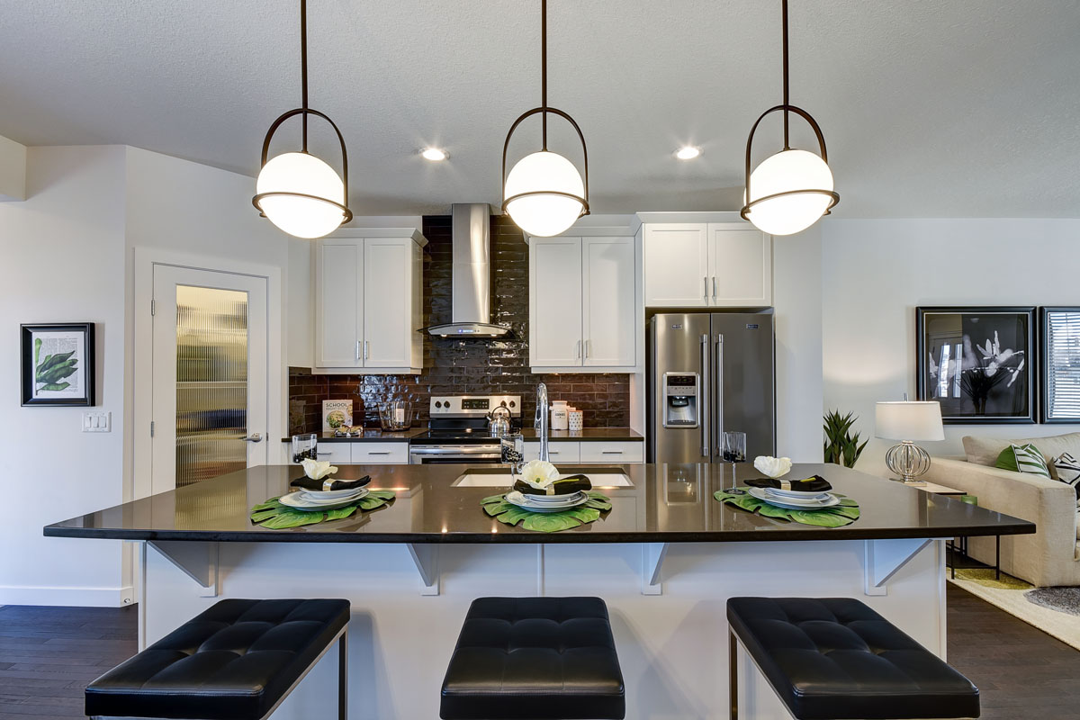 Front view of the kitchen in the Banbury ll model home from Nuvsita Homes. Plates and cutlery placed on the island table with low hanging custom lights.