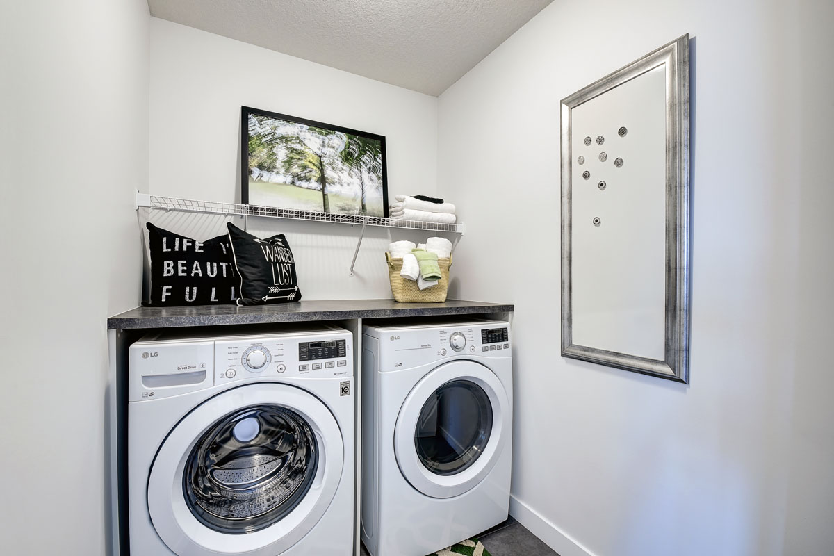 Laundry room with white LG washer and dryer. decrotive painting and basket on top of counter in the Banbury II model home from Nuvista Homes.