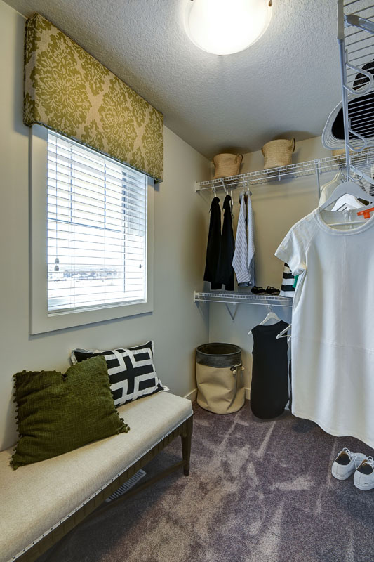 walk in closet with clothes on hangers and a bench with decrotive throw pillows. Banbury ll model home from Nuvista Homes.