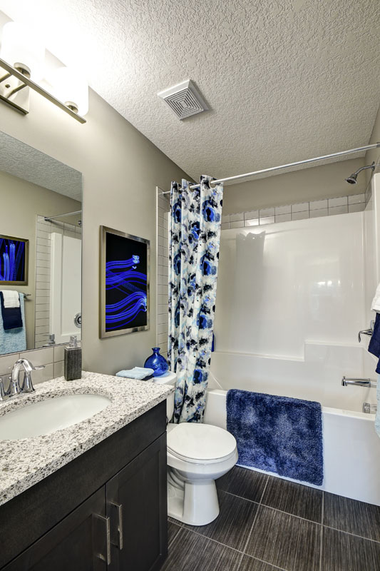Bathroom with a blue shower curtian and blue floor mat in the Banbury ll model home from Nuvista Homes.