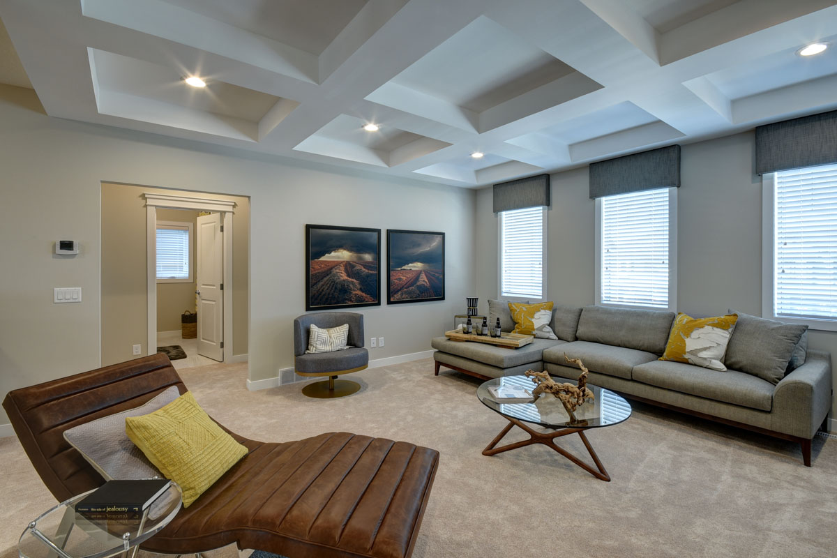 Bonus room with large grey sectional across from brown leather chair and round glass coffee table in the Bentley II model home.