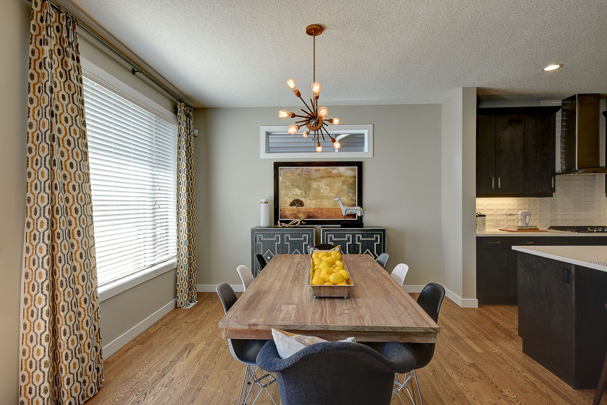 Dining room with large table and six chairs next to window with yellow and blue curtians in the Bentley II model home.
