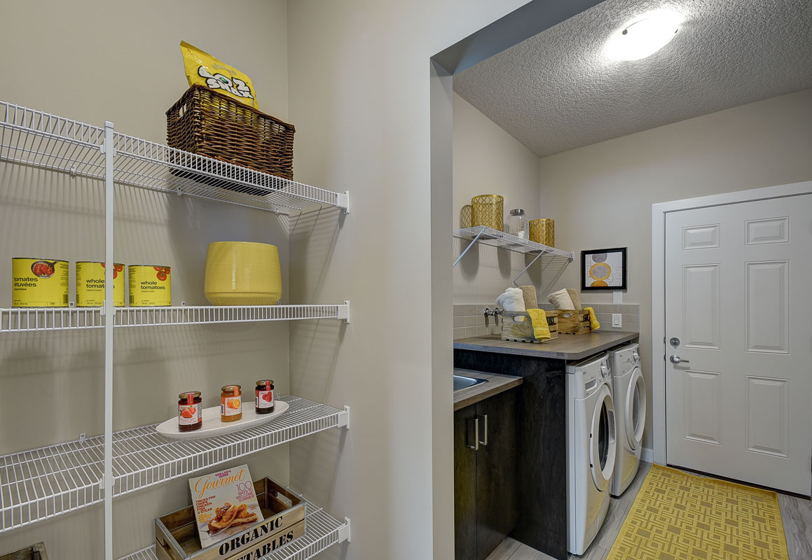 Pantry next to the laundry room in the Bentley II model home with white shelving and cooking supplies.
