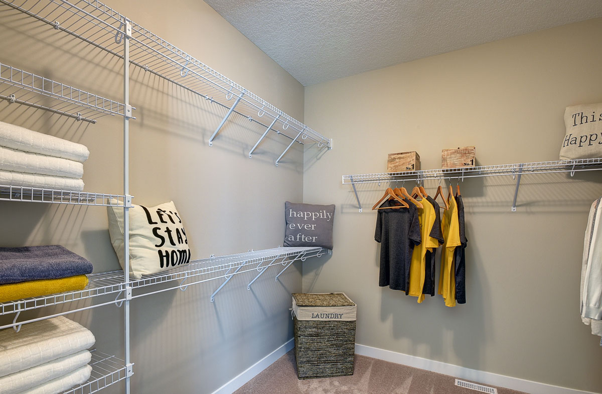 Walk in closet in the Bentley II model home from Nuvista homes with white shelving and clothes hanging up.