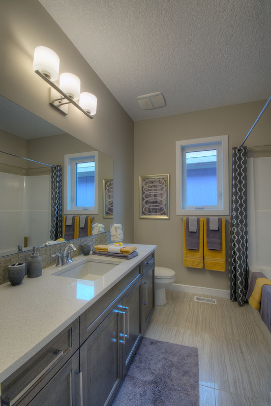 Bathroom in the Bentley II model home with grey vanity across from shower with yellow and grey accent towels.