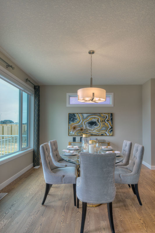 Dining room next to large bay window with long glass table and 6 plush chairs in the Bentley II model home.