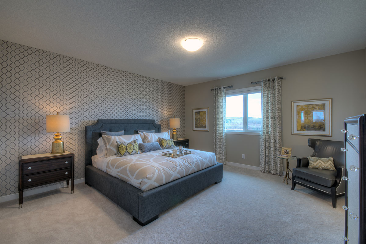 Master bedroom with king bed and beige accent wall and blue leather arm chair in the Bentley II model home.
