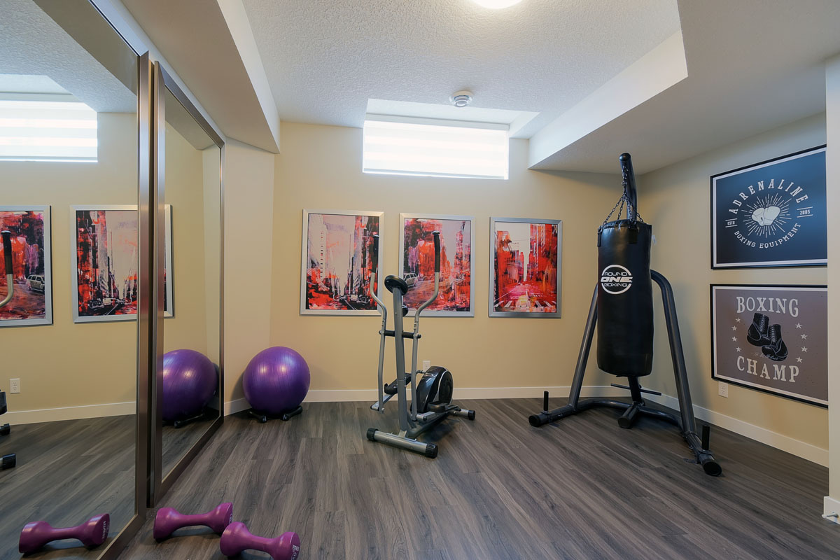 Basement gym with dark wood flooring and a elliptical next to punching bag in the Brentwood model home.