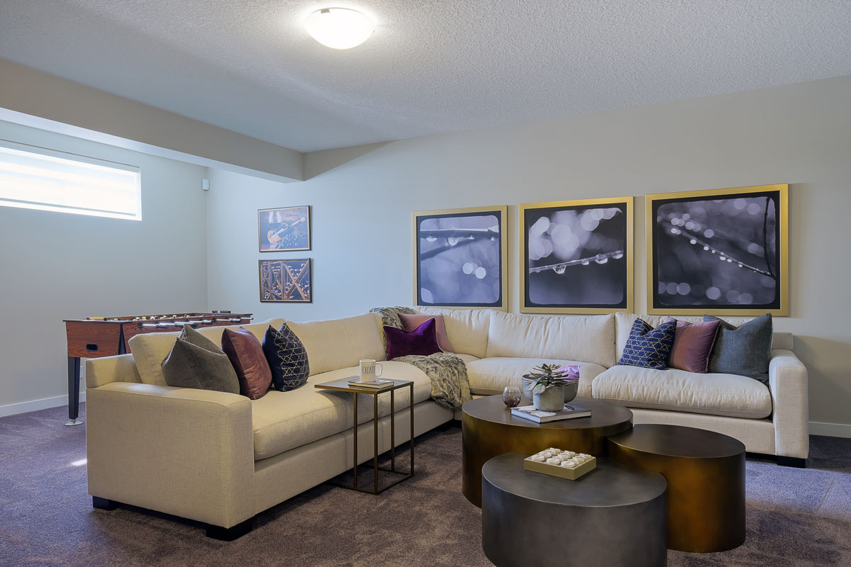 Basement living room in the Brentwood model home with white sectional and three round multi level coffee tables.
