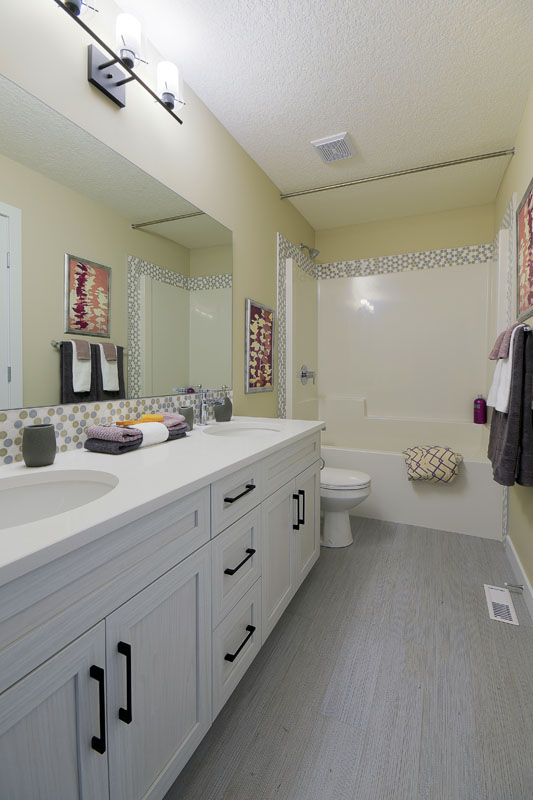 Bathroom with double white vanity and light grey wood flooring next to toliet and shower in the Brentwood model home.