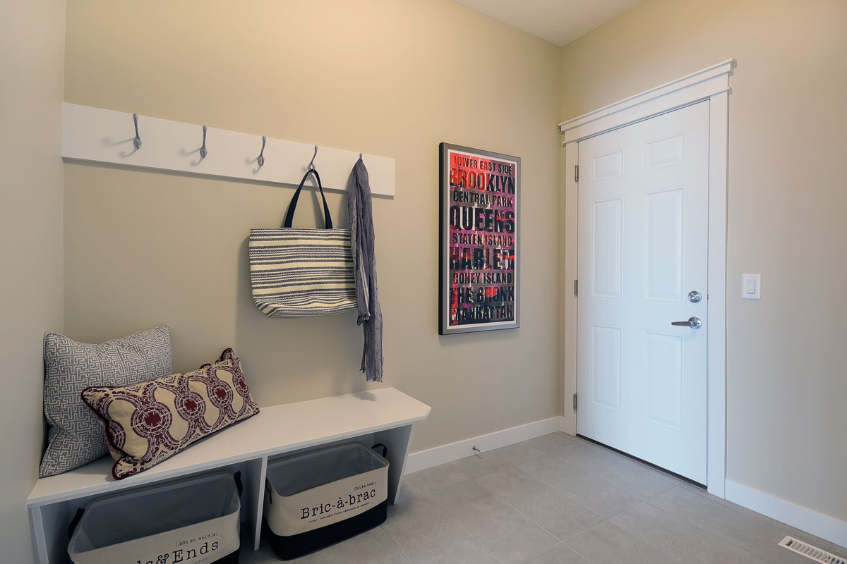 Mudroom with grey tile flooring next to built in white bench and hangers in the Brentwood model home.