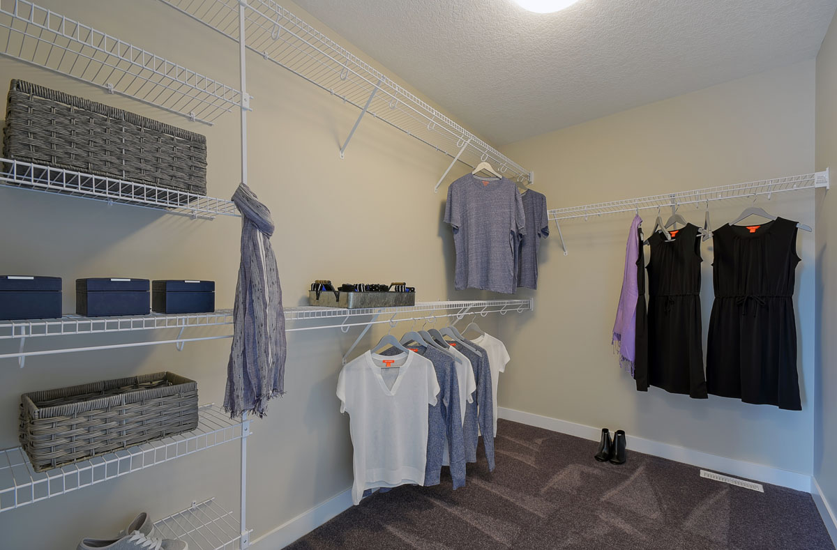 Walk in closet in the Brentwood model home with white shelving and clothes haning up.