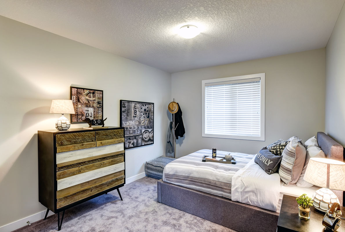 Bedroom one with a modern wood style dresser and a queen bed in the Hamilton Wil model home.