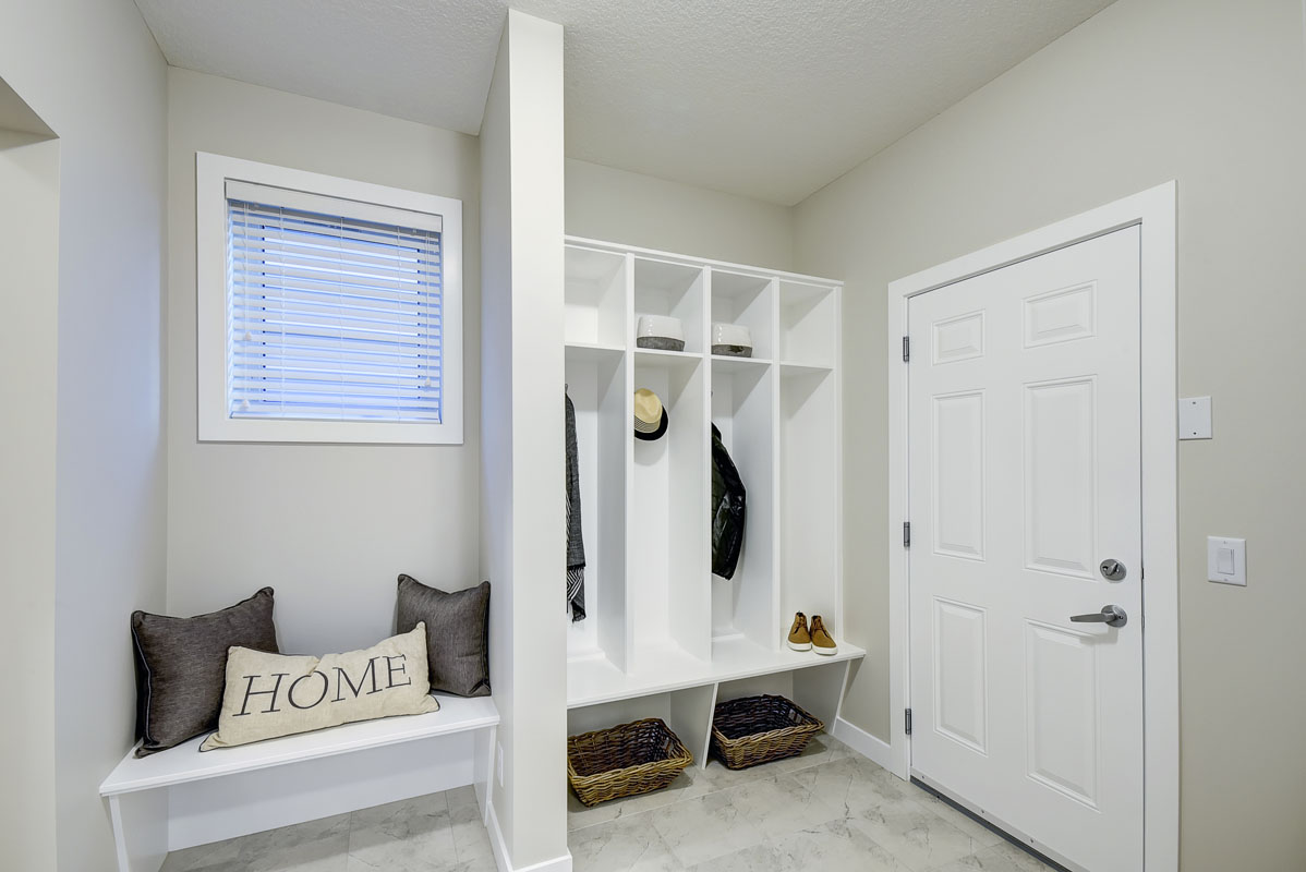 Mudroom with a white bench and white cabinets and decrotive throw pillows in the Hamilton Wil model home.