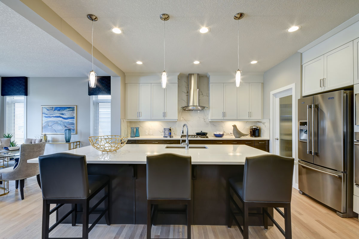Kitchen with stainless steel appliances and three chairs next to the island in the Inverness Red model home.