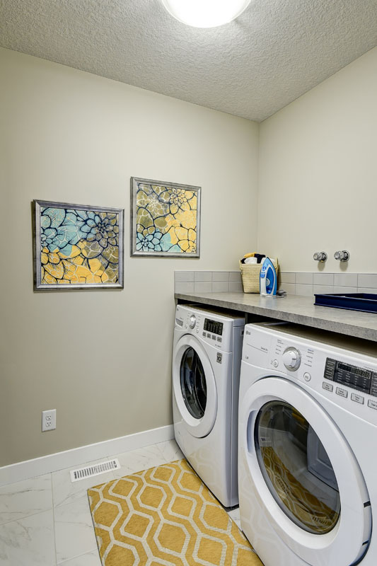 Laundry room with yellow mat and decrotive floral photos next to white LG washer and dryer.