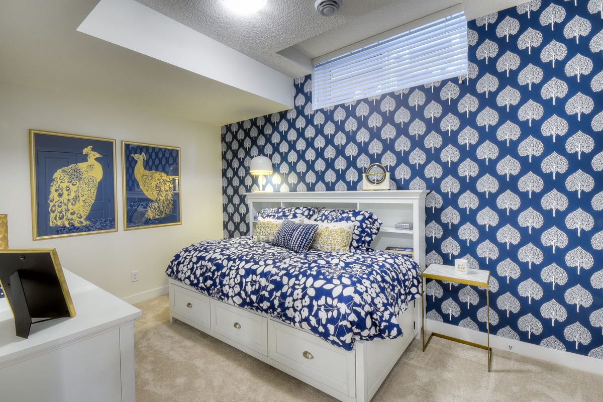 Basement bedroom with leaf print blue and white accent wall and twin bed on white frame in the Kingsley Cre model home.