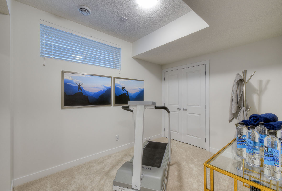Basement gym with treadmill and table with water bottles in the Kingsley Cre model home.