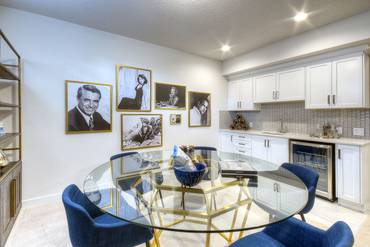 Wet bar in the basement of the Kingsley Cre model home with large round glass table and five blue chairs.