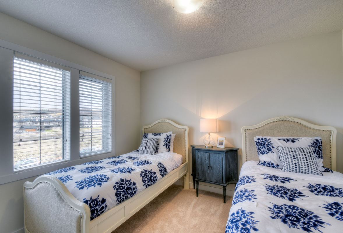 Bedroom two with two twin beds and white and blue matching bedding in the Kingsley Cre model home.