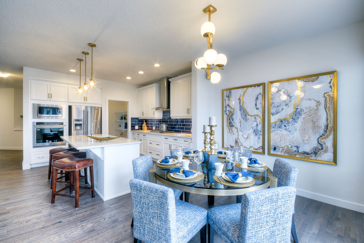 Dinning room next to kitchen with a round glass table and six blue chairs in the Kingsley Cre model home.