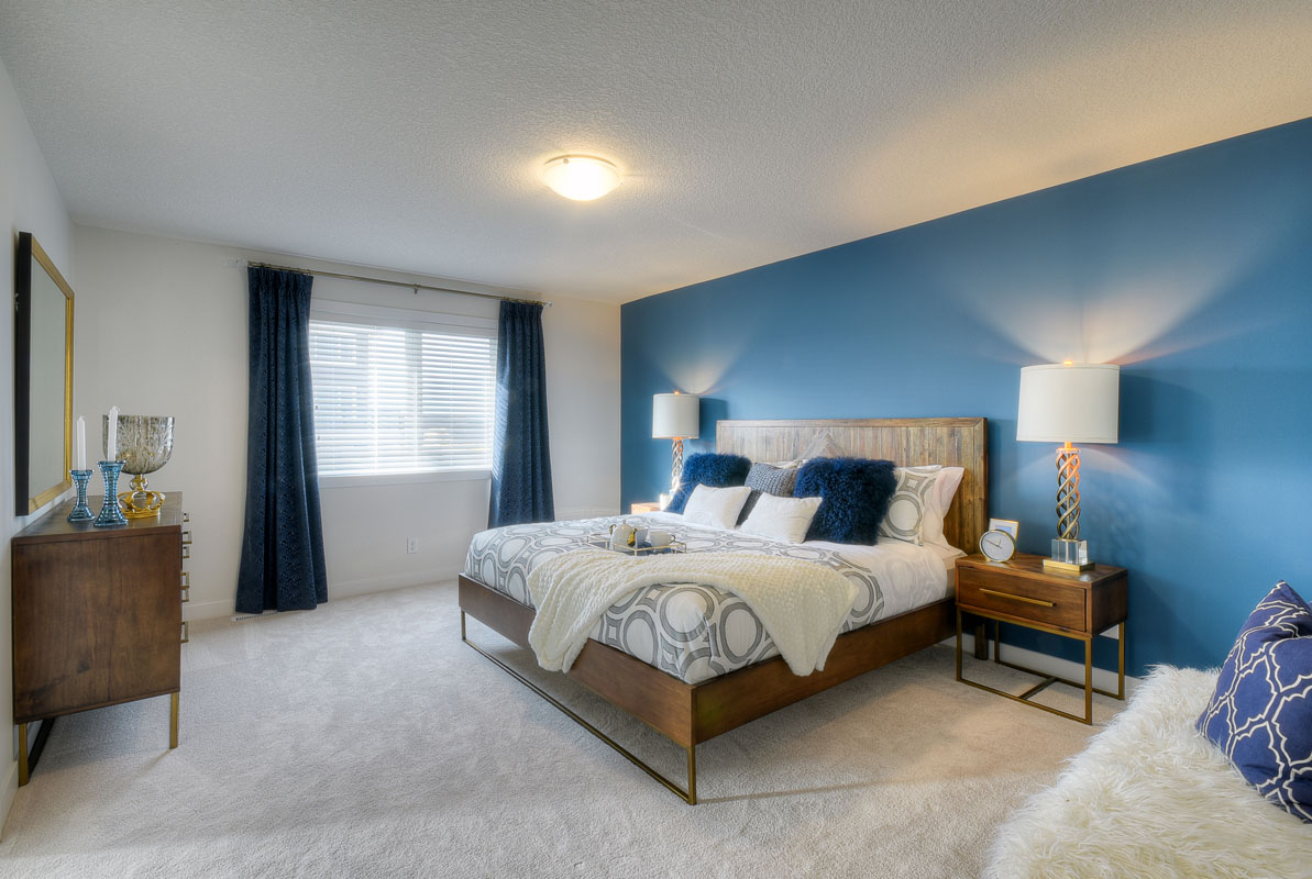 Master bedroom with blue accent wall and kingsize bed on wood frame in the Kingsley Cre model home.