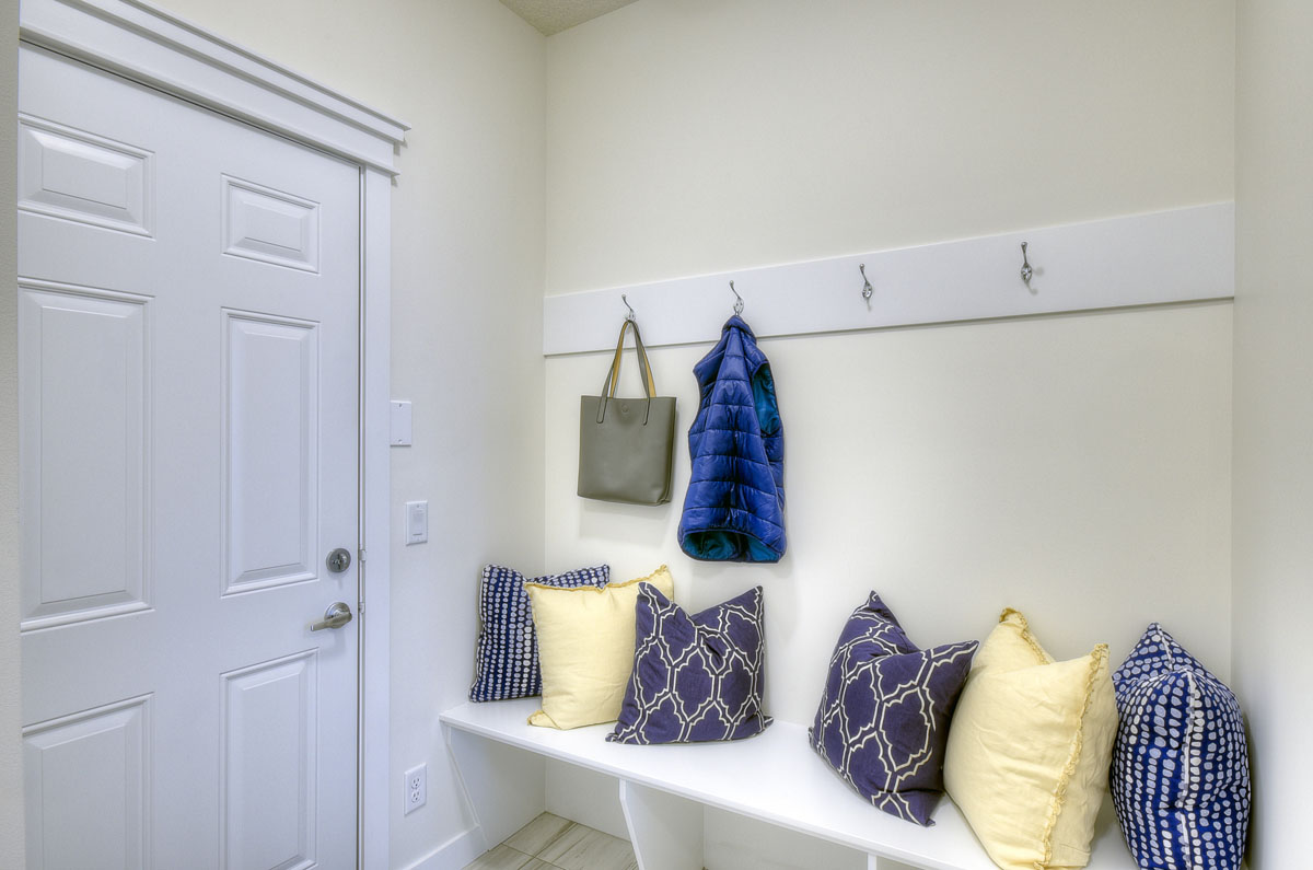 Mudroom with white bench and yellow and blue throw pillows in the Kingsley Cre model home.