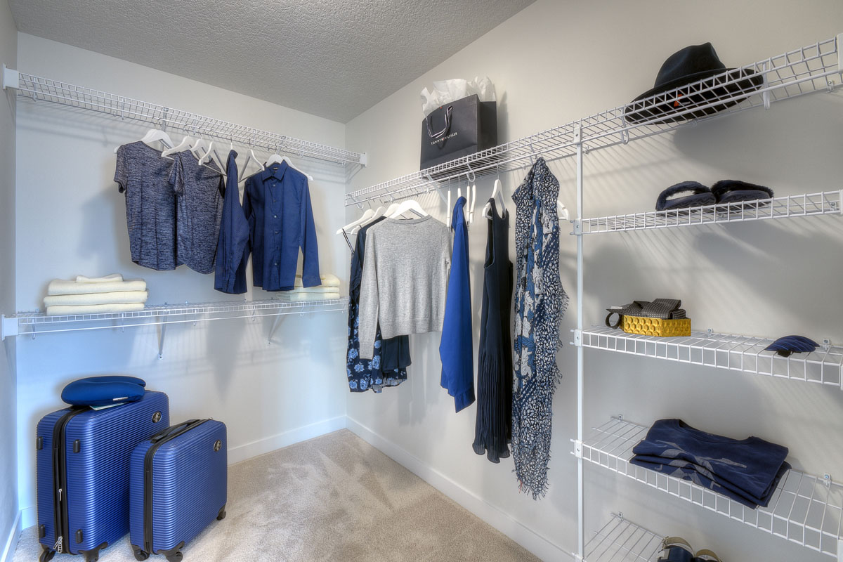 Walk-in closet with blue lugage and womens clothes hanging up in the Kingsley Cre model home.