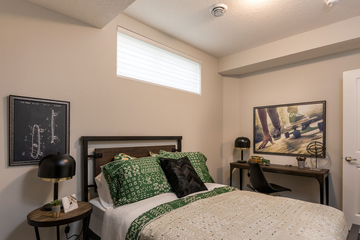second basement bedroom with round wood nightstands and green pillows on queen bed in the Kingston model home.