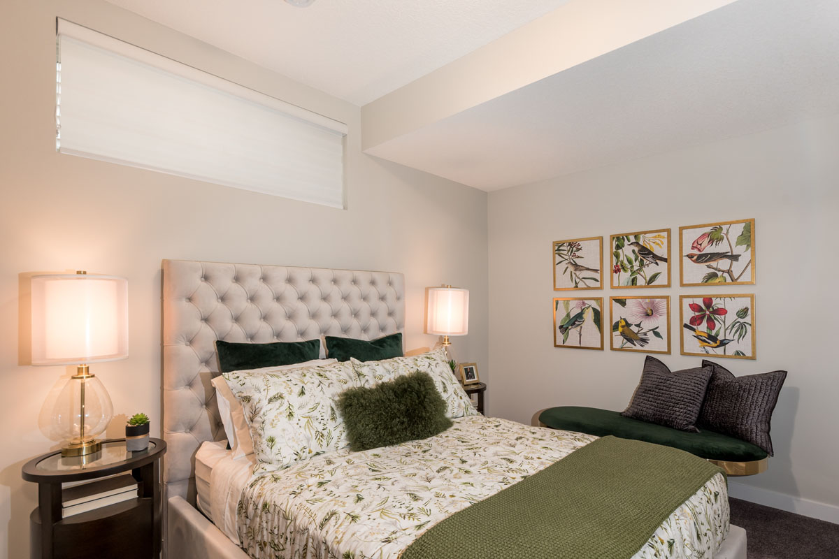Basement bedroom with queen bed and green comforter and matching round nightstands in the Kingston model home.