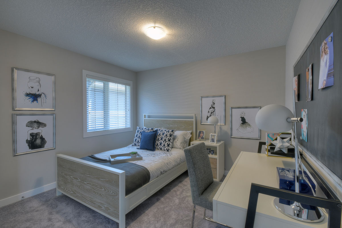 Bedroom one in the Kirkwood model home with a twin bed made with white floral bedding and a white desk with a grey chair.