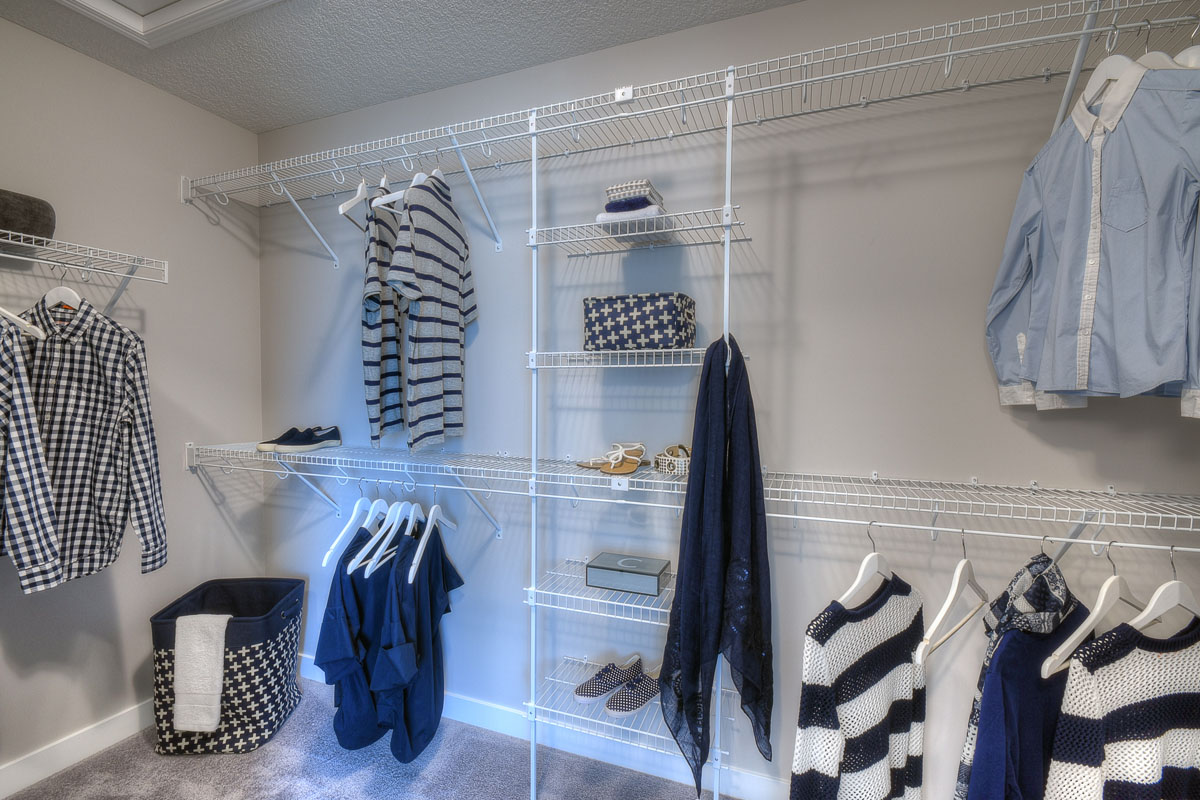 Walk in closet with mens and womens clothes hanging up in the Kirkwood model home from Nuvista Homes.