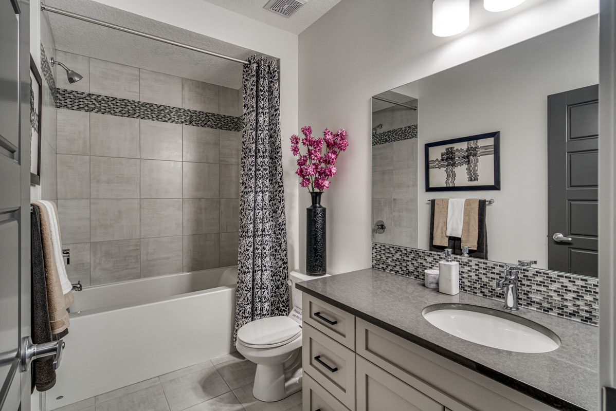 Basement bathroom with white vanity and blakc and white print shower curtain in the Lakeview model home.