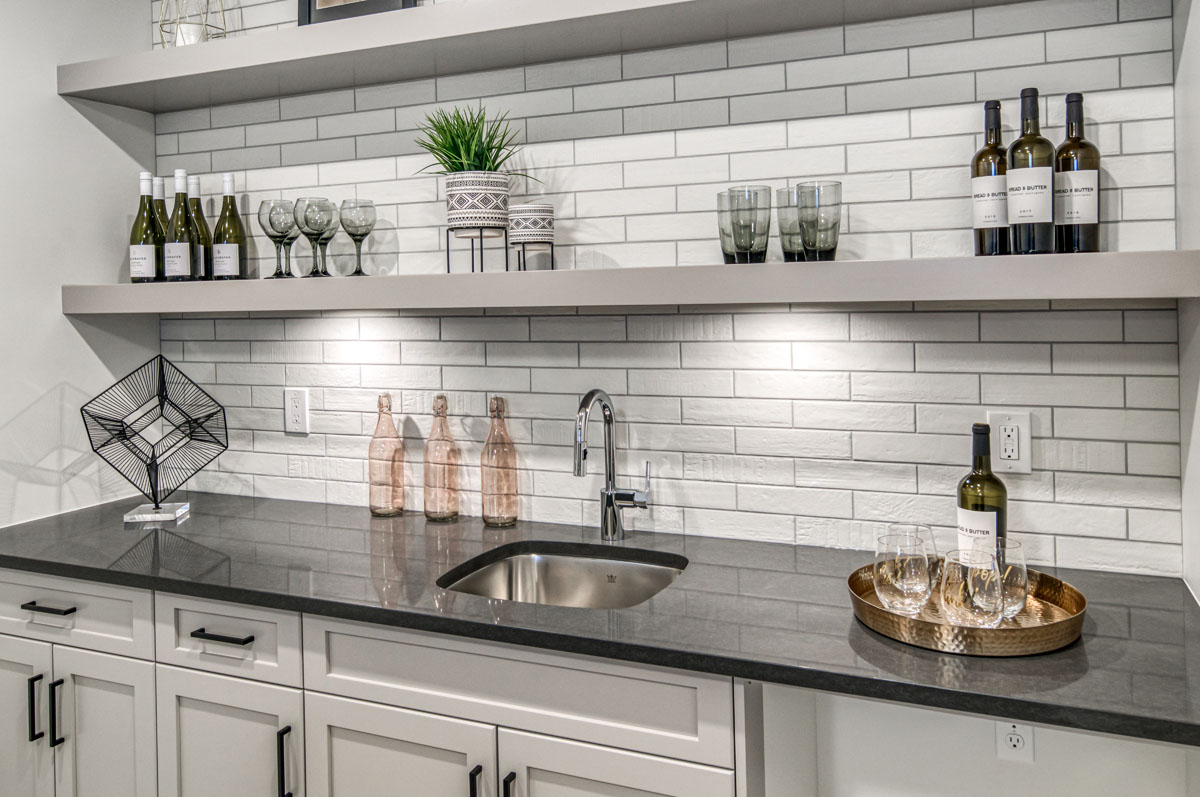Wet bar in the Lakeview model home with grey granite countertops and white cupboards.
