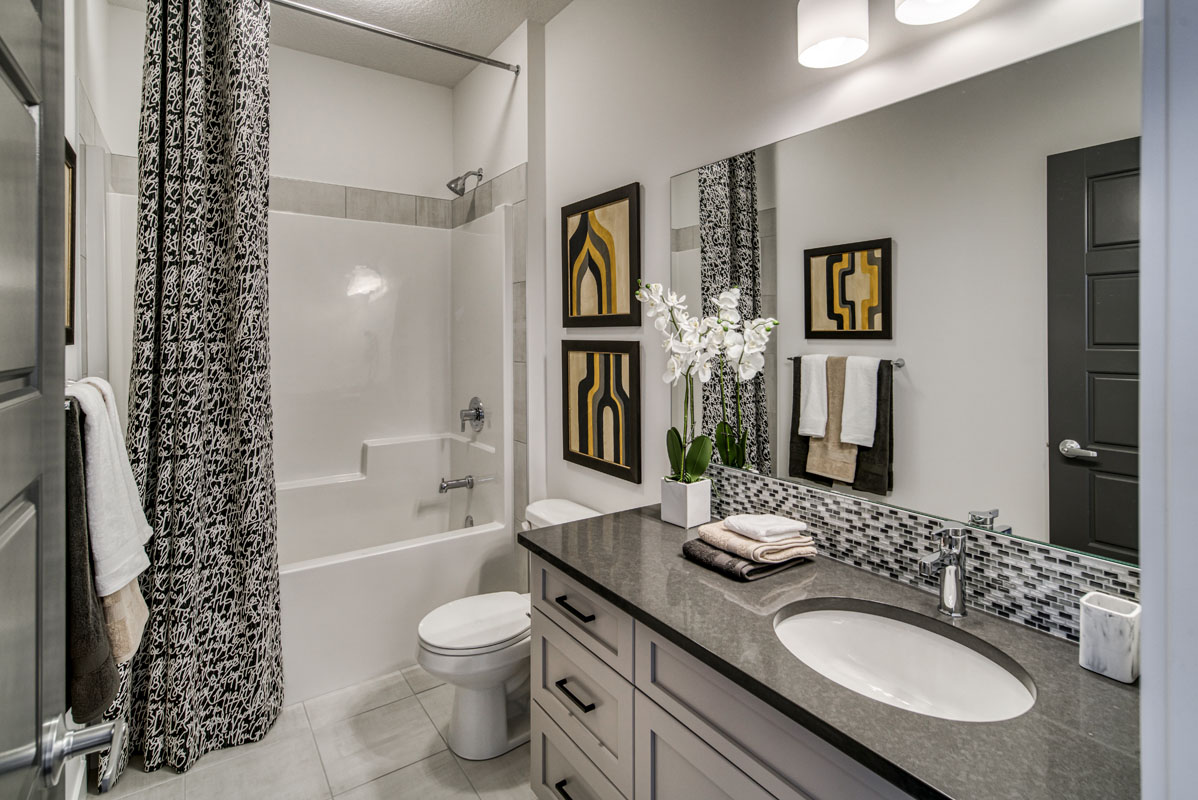 Bathroom with white vanity and grey countertop next to toliet and shower in the Lakeview model home.