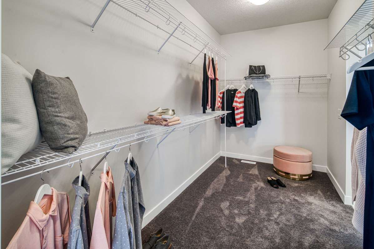 Walk in closet in the Lakeview model home with white shelving and dark grey carpeting.