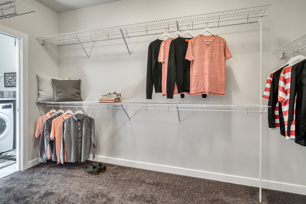 Walk in closet next to laundry room in the Lakeview model home with white shelving and clothes hanging up.