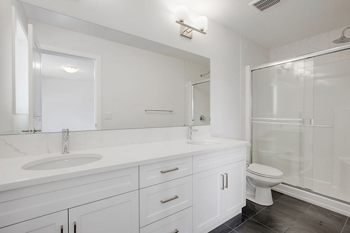 Upstairs bathroom in the Maybank model home with double white vanity and sliding shower doors.