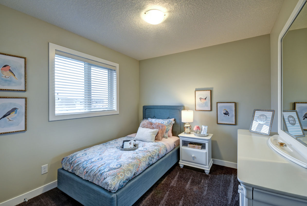 Second bedroom in the NuHaven II model home with twin bed across from white dresser and dark grey carpet flooring.