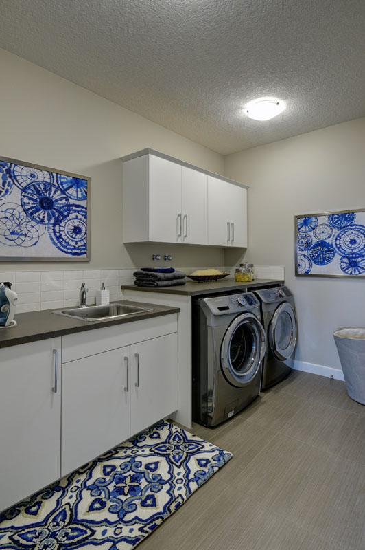 Laundry room with large counter and sink next to matching washer and dryer in the Cayenne model home.