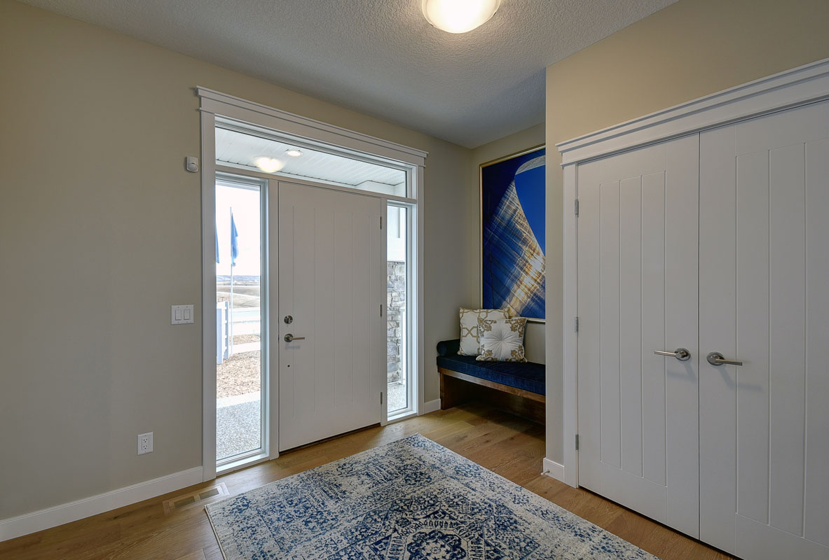 Front foyer in the Cayenne model home with large white and blue print rug and closet next to blue bench.