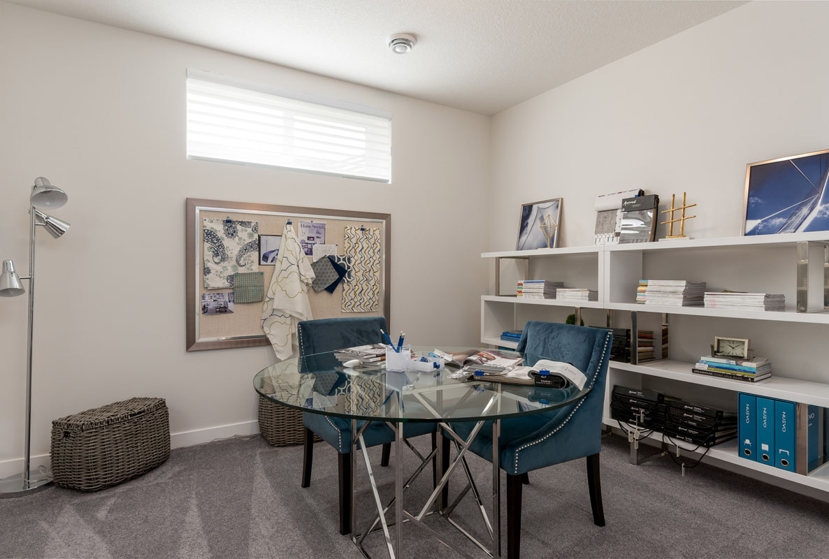 basement area of the Wilshire model home with round glass table and two blue swede chairs and large white shelving.