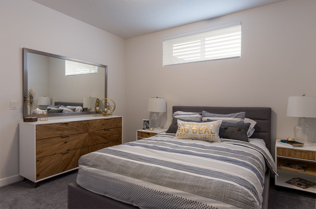 Basement bedroom in the Wilshire model home with queen size bed and large modern wood dresser and mirror.