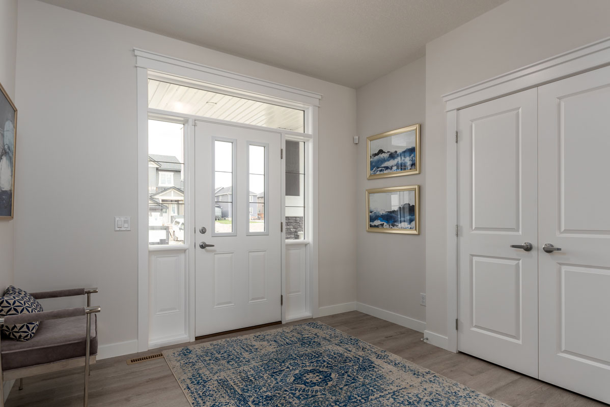 Main foyer in the Wilshire model home with large blue and white area rug and silver chair next to door.