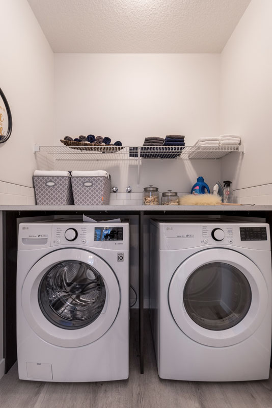 Laundry room with white LG washer and dryer and countertop with cleaning supplies in the Wilshire model home.